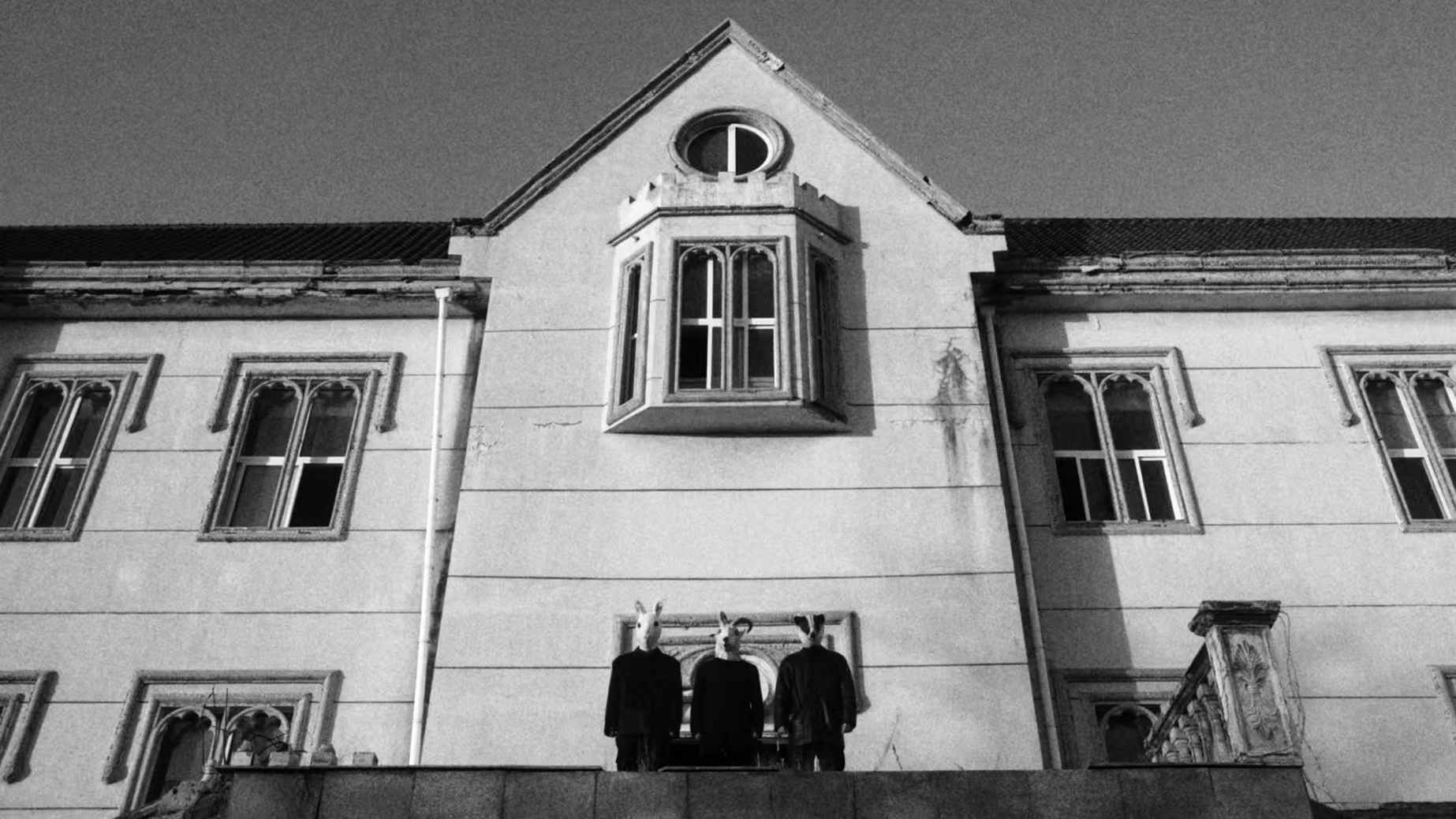 Three masked figures outside a large building