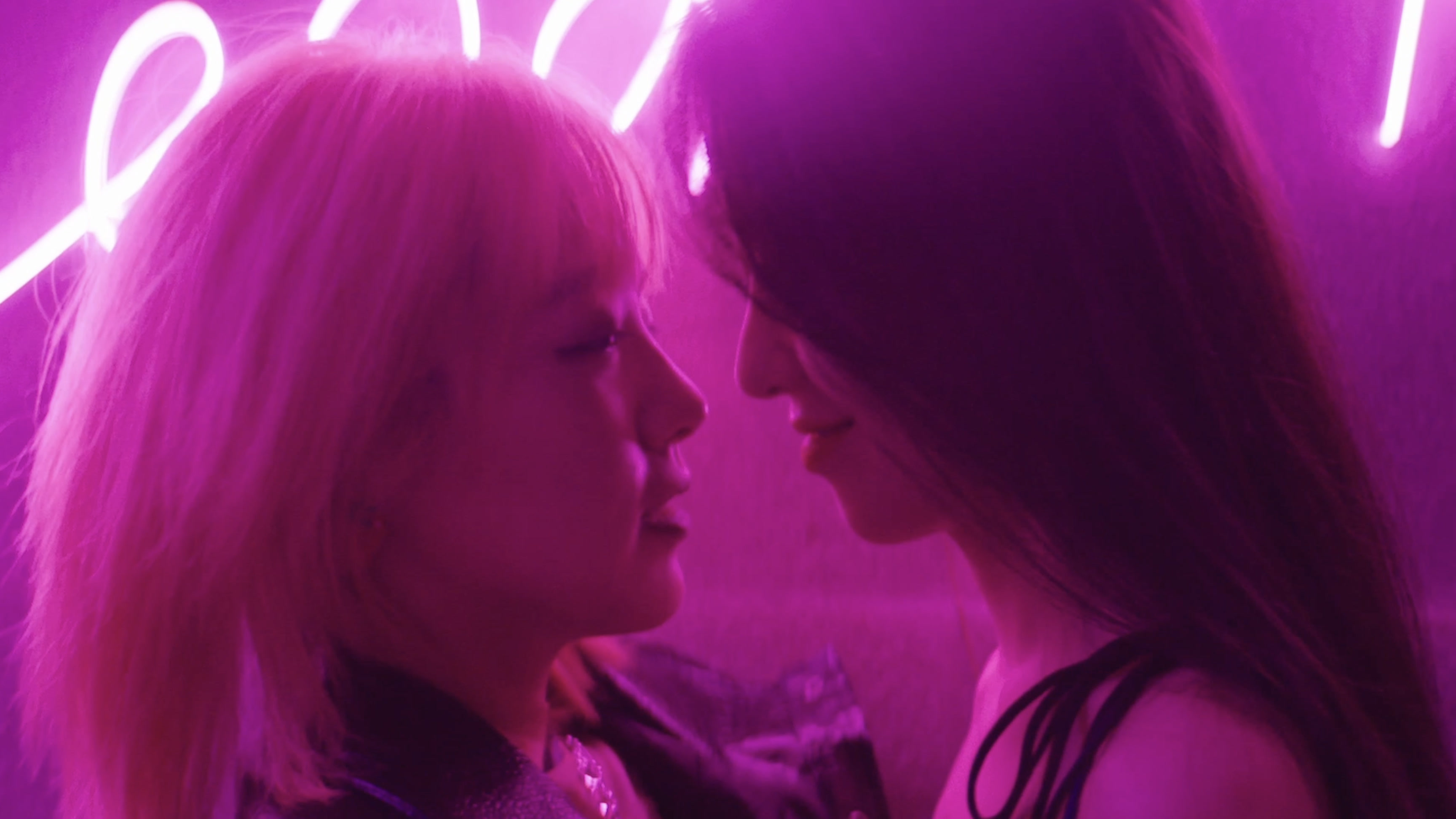 Two girls beneath pink neon light