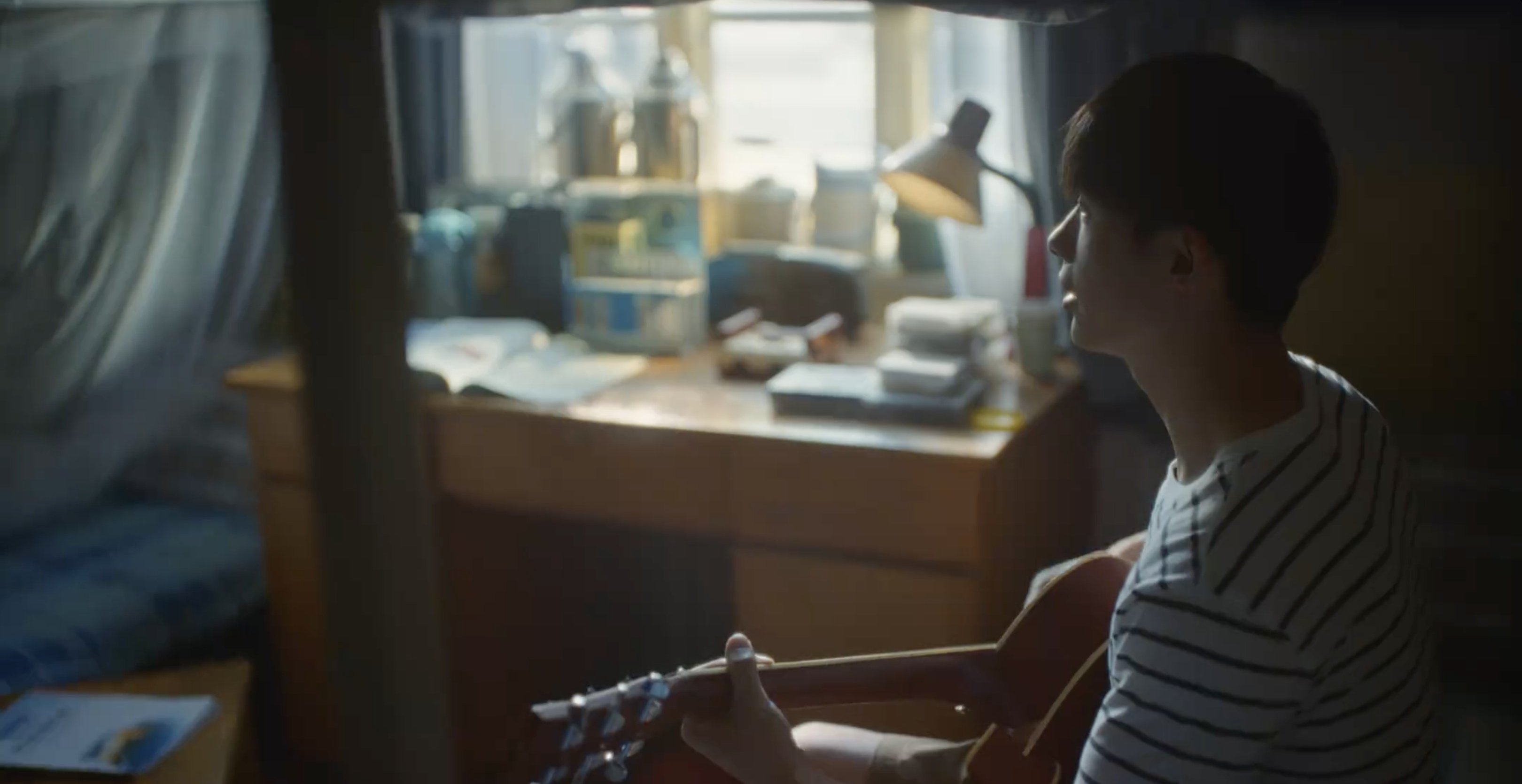 A young man playing guitar beside a bedroom window